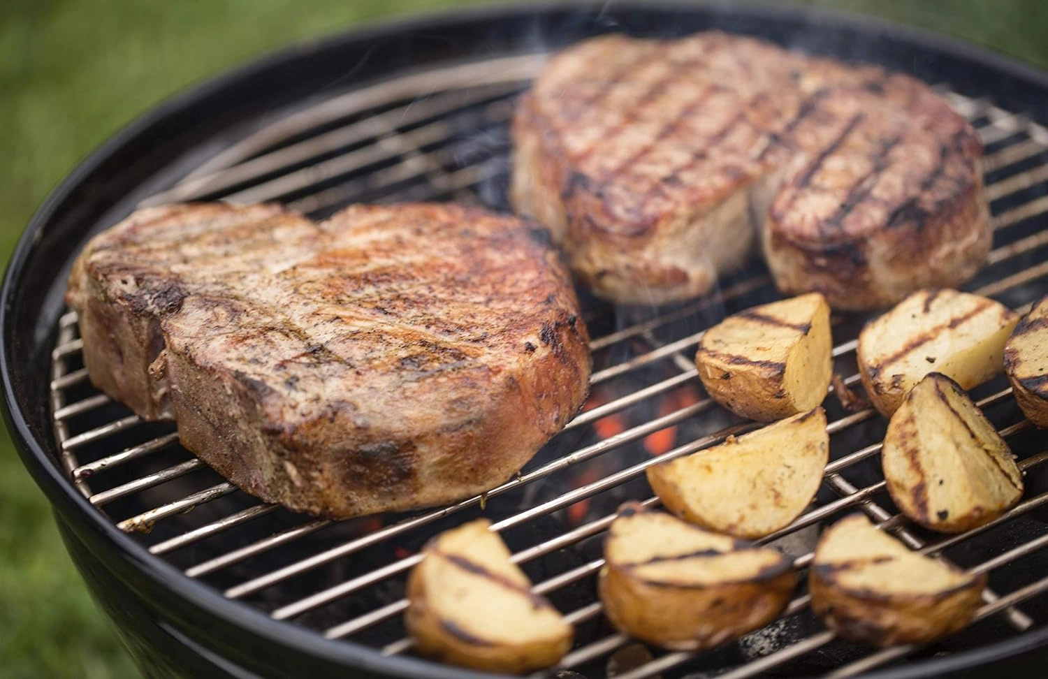 Doua bucati de carne si bucati de cartofi pe grilajul gratarului pe carbuni Smokey Joe Gri